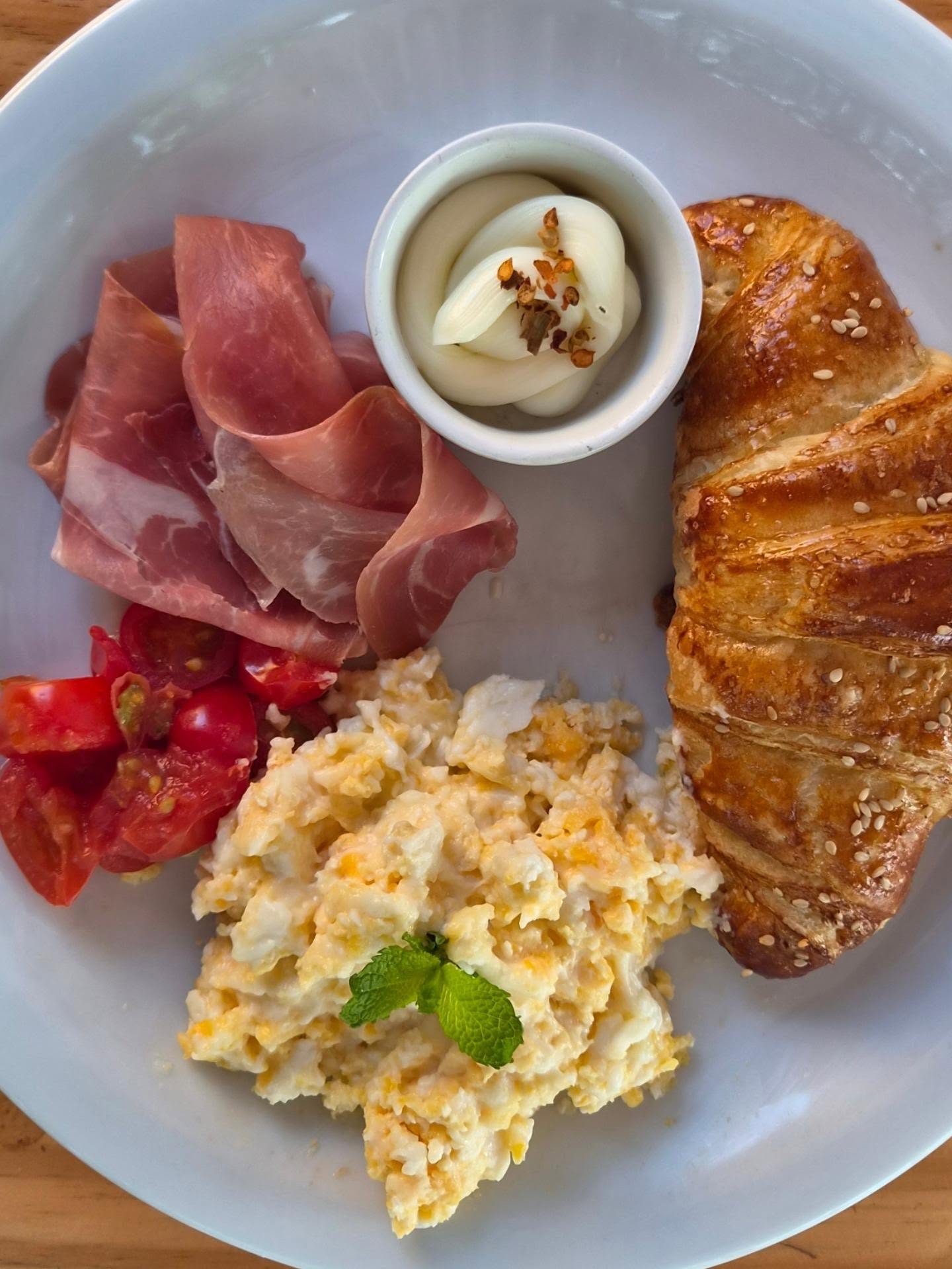 Croissant dourado servido com presunto de parma, requeijão e tomatinhos